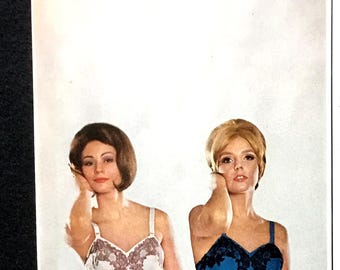 May include: Vintage advertisement featuring two women modeling nylon tricot chemise slips. One woman wears a white slip with brown lace, the other a blue slip with black lace. The ad promotes Beaunit nylon tricot.