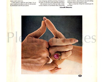 May include: A close-up of two hands clasped together, with a large red gemstone ring on the right hand's ring finger. The ring is set in gold and has smaller diamonds surrounding the gemstone. The text "The wishing star." is at the top of the image, and the text "Lindé Stars" is at the bottom of the image.