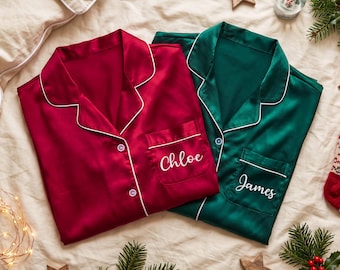Puede incluir: Dos camisas de pijama abotonadas de manga larga con cuello de solapa. Una camisa es de color rojo oscuro con el nombre Chloe bordado en blanco en el bolsillo del pecho, y la otra es de color verde oscuro con el nombre James bordado en blanco.