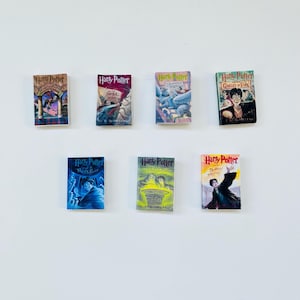 May include: A collection of miniature "Harry Potter" book replicas. Each book features a different cover design with vibrant colors and illustrations, showcasing various scenes and characters from the series.