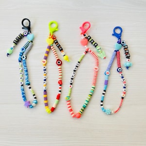 May include: Four colorful beaded keychains with personalized names, including "Leo", "Katie", "Sabrina", and "Mary", each featuring a charm and a small heart. The keychains are made with colorful beads, including rainbow, pink, blue, and green.