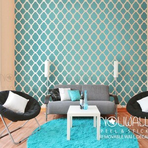 Peut inclure: Un autocollant mural amovible pelable et repositionnable à motif géométrique bleu sarcelle et blanc. L'autocollant est appliqué sur un mur dans un salon avec un canapé, deux chaises, une table basse et un tapis.