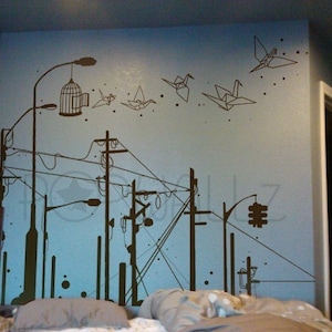 May include: A bedroom wall with a brown silhouette of a city skyline with streetlights and power lines. The wall also features a brown birdcage and several origami paper cranes in flight.