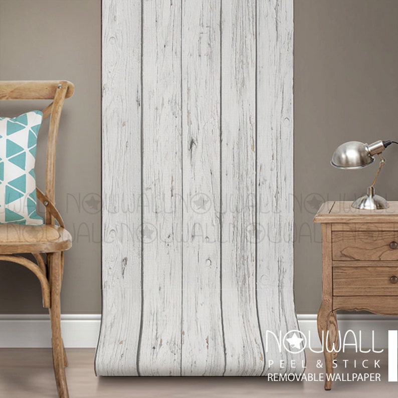 May include: Whitewashed wood peel and stick wallpaper with a distressed look. The wallpaper is shown rolled out on a wooden floor next to a wooden chair and a wooden nightstand. The text "NOWALL PEEL & STICK REMOVABLE WALLPAPER" is visible at the bottom of the image.