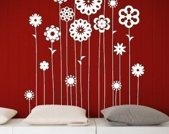 May include: White silhouette of stylized flowers on a red background. The flowers are arranged in a row and have different shapes and sizes. The flowers are on a wall behind a white couch with two pillows.