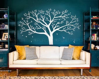 May include: A white tree decal on a teal wall with a white couch and two teal bookshelves on either side. The couch has two pillows, one yellow and one gray.