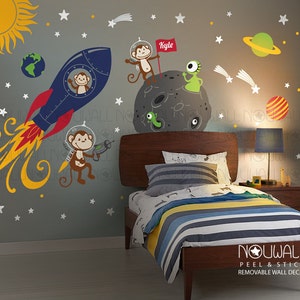 May include: A set of peel and stick wall decals featuring a rocket, monkeys, a planet, stars, and the name "Kyle". The decals are on a gray wall in a child's bedroom.