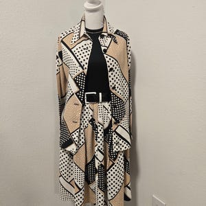May include: A long-sleeved button-down shirt and a matching midi skirt featuring a geometric pattern of black, white, and tan polka dots and solid blocks. The outfit is worn over a black ribbed top and cinched with a black belt featuring a white buckle.