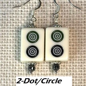 May include: Earrings with rectangular white tiles, each displaying green and black concentric circles. The earrings have silver hooks and hematite bead details. The text "2-Dot/Circle with Hematite" is visible below the earrings.