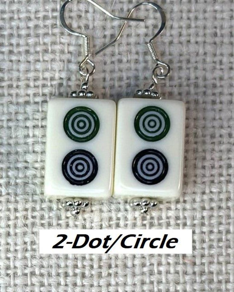 May include: Earrings with rectangular white tiles, each displaying green and black concentric circles. The earrings have silver-coloured hooks and decorative details. The text "2-Dot/Circle" is visible below the earrings.