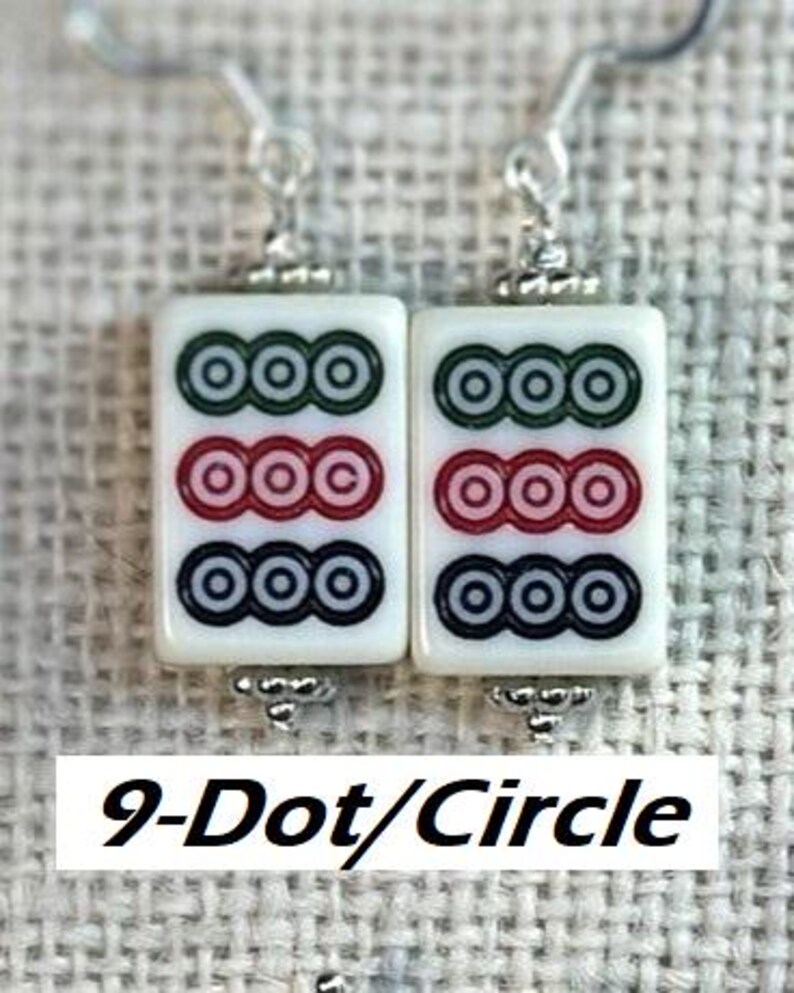 May include: A pair of white Mahjong tile earrings, each featuring three rows of circles in green, red, and black. The earrings have silver-coloured hooks and decorative accents. The text "9-Dot/Circle" is displayed below the earrings.
