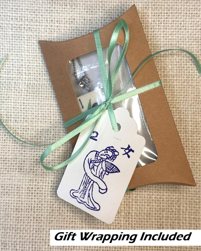 May include: A small, brown gift box with a clear window, tied with a light green ribbon. Inside is a silver necklace. A white tag with a blue illustration of a woman and Chinese characters is attached.