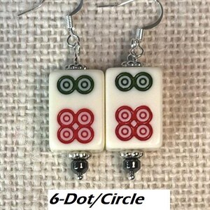 May include: A pair of earrings with rectangular white tiles, each displaying green and red circle patterns. The earrings have silver hooks and are labelled "6-Dot/Circle with Hematite."