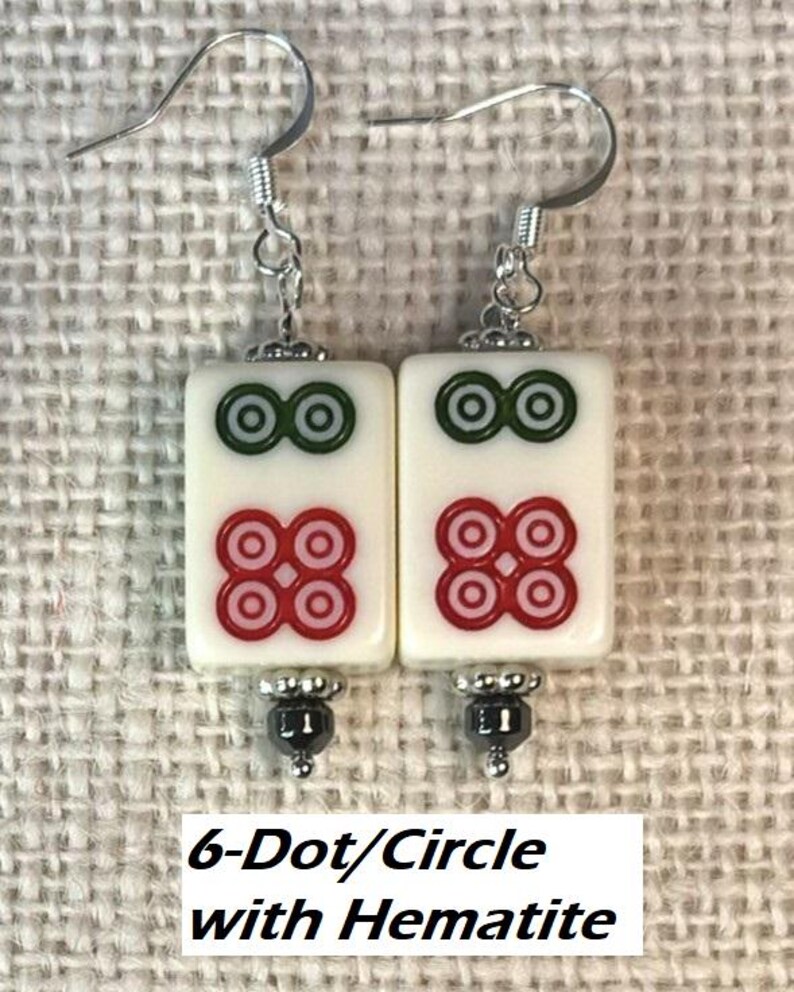 May include: A pair of earrings with rectangular white tiles, each displaying green and red circle patterns. The earrings have silver hooks and are labelled "6-Dot/Circle with Hematite."