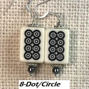 May include: A pair of earrings with rectangular white tiles, each displaying a black and white 8-dot pattern. The earrings have silver hooks and hematite bead accents.