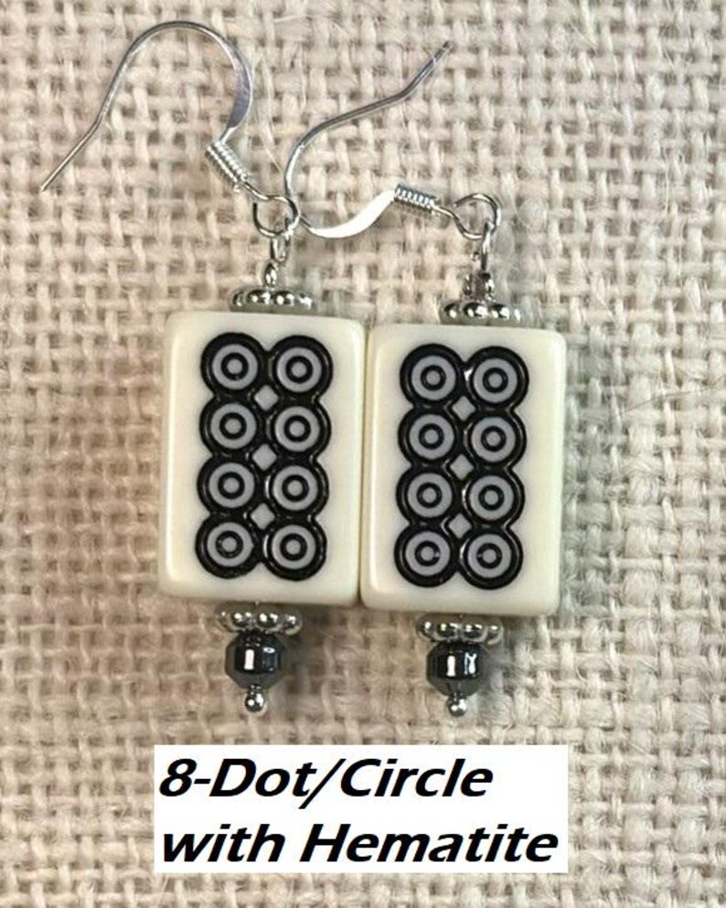 May include: A pair of earrings with rectangular white tiles, each displaying a black and white 8-dot pattern. The earrings have silver hooks and hematite bead accents.
