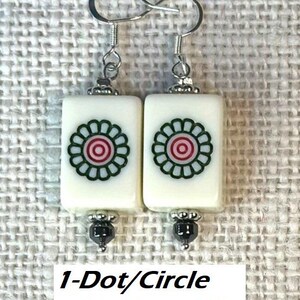 May include: Earrings with rectangular white tiles, each displaying a green and red floral motif. The earrings have silver-tone hooks and hematite bead accents. The text "1-Dot/Circle with Hematite" is visible.