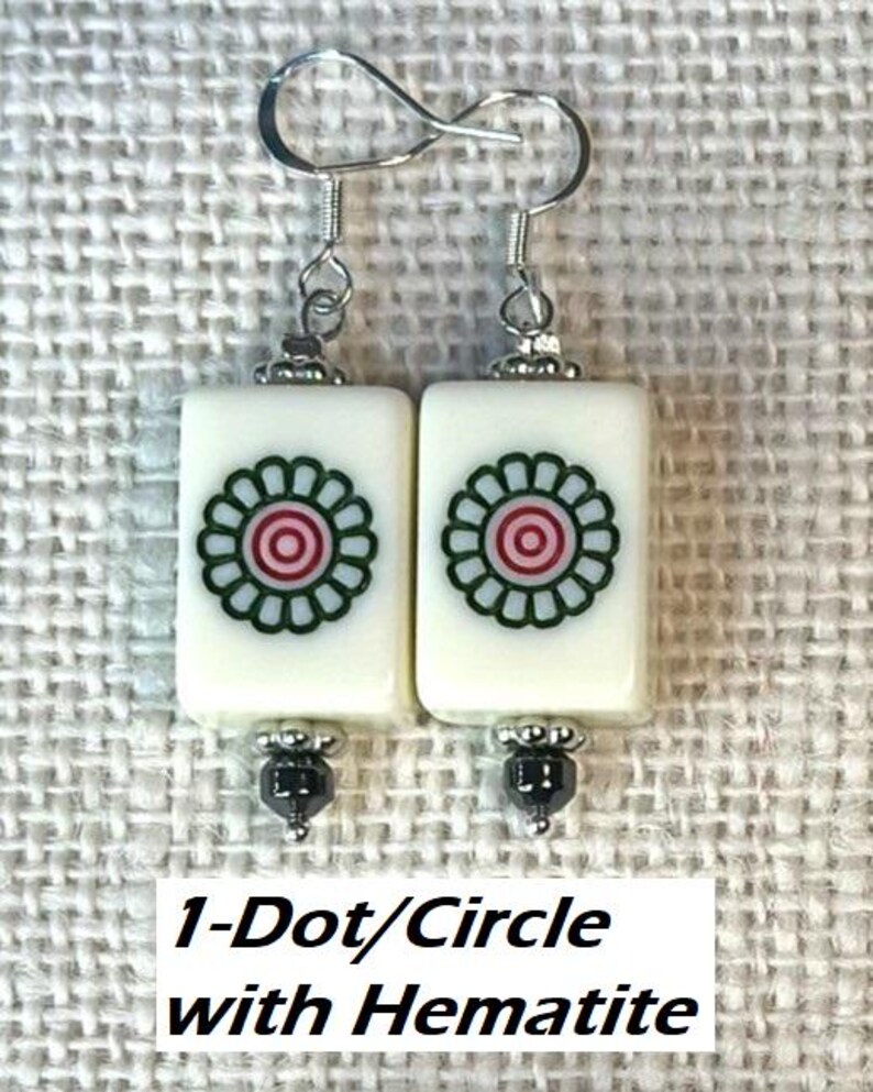 May include: Earrings with rectangular white tiles, each displaying a green and red floral motif. The earrings have silver-tone hooks and hematite bead accents. The text "1-Dot/Circle with Hematite" is visible.