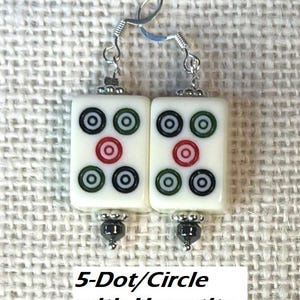 May include: A pair of white rectangular earrings featuring a 5-dot/circle design in black, green, and red. They have silver-tone hooks and hematite bead accents. The text "5-Dot/Circle with Hematite" is at the bottom.