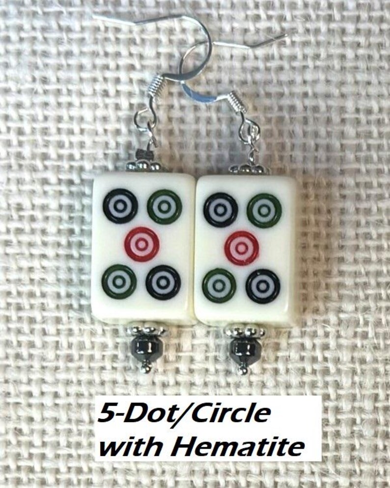 May include: A pair of white rectangular earrings featuring a 5-dot/circle design in black, green, and red. They have silver-tone hooks and hematite bead accents. The text "5-Dot/Circle with Hematite" is at the bottom.