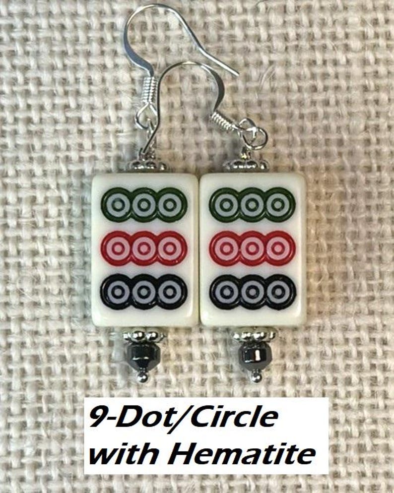 May include: Earrings with white rectangular tiles, each displaying three rows of three circles in green, red, and black. Silver hooks and hematite beads complete the design. The text "9-Dot/Circle with Hematite" is visible at the bottom of the image.