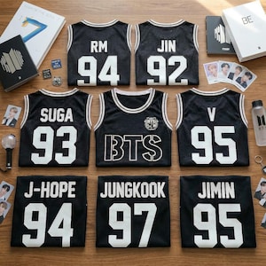 May include: Black basketball jerseys with white trim and lettering, featuring names and numbers. The jerseys are arranged with BTS merchandise, including albums, photo cards, and a water bottle. The numbers on the jerseys are 92, 93, 94, 95, and 97.