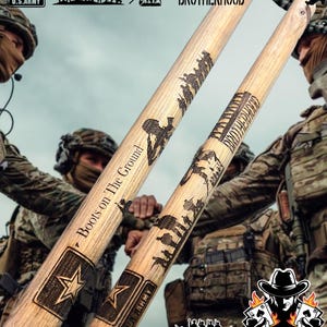 May include: Two wooden baseball bats with a military theme. The bats are engraved with the words "Boots on The Ground" and a silhouette of soldiers. The bats also feature the U.S. Army star and the words "Brotherhood".