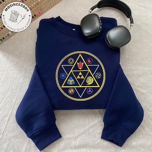 May include: Navy blue sweatshirt featuring a colorful geometric design with a triangle at the center. The design is surrounded by a circle with various symbols. A pair of black headphones rests on the sweatshirt.