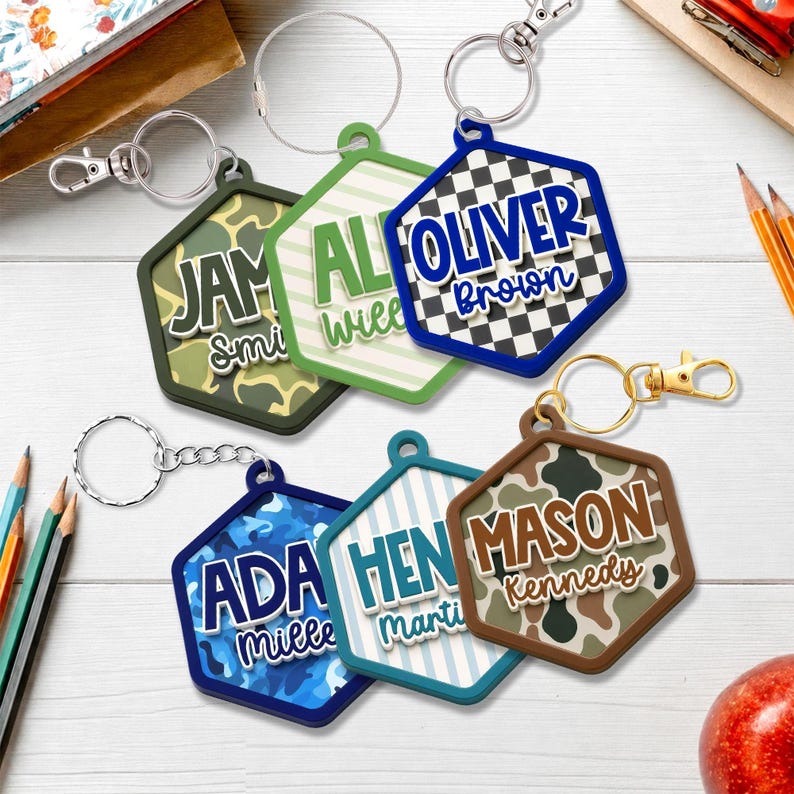 May include: Six hexagonal keychains with metal lobster claw clasps and split rings. Each features a unique background pattern including camouflage, stripes, and checkers, with raised white and colored lettering displaying names like Oliver Brown and Mason Kennedy.