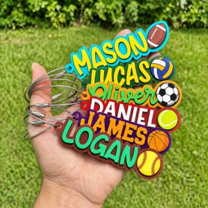 May include: A set of six colorful acrylic bag tags featuring the names Mason, Lucas, Oliver, Daniel, James, and Logan. Each tag is paired with a specific sports ball icon including a football, volleyball, soccer ball, tennis ball, and basketball.