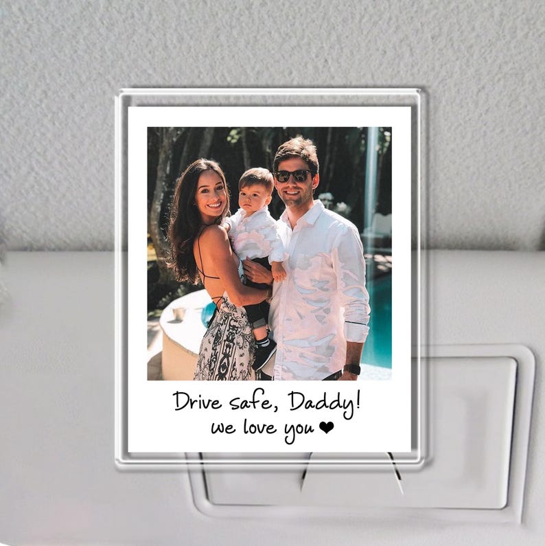 Puede incluir: Un marco de fotos transparente de acr&iacute;lico con un retrato familiar. La foto muestra a una mujer, un hombre y un ni&ntilde;o. El texto en la foto dice "Drive safe, Daddy! we love you". El marco se muestra sobre un fondo neutro.