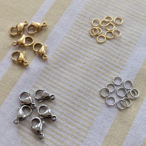 May include: A collection of gold and silver jump rings and lobster clasps. The jump rings are small and round, while the lobster clasps are silver and have a spring-loaded opening.
