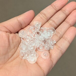 May include: A pile of clear plastic earring backs. The backs are small and round with a small nub on the back.