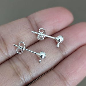 May include: Two silver earring posts with a small ball at the end. The posts are designed to be used with a variety of charms and pendants.
