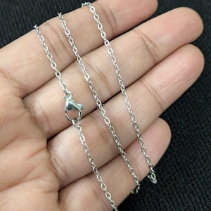 May include: A silver chain necklace with a lobster clasp closure. The chain is shown on a hand, with the chain laying flat.