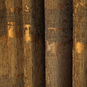 May include: Close-up of textured fabric with vertical stripes in shades of gold and dark brown. The fabric has a subtle sheen and a pattern of irregular gold shapes, creating a luxurious appearance. The folds add depth and dimension to the textile.