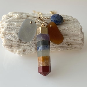 May include: A gold chain necklace with a multi-colored crystal pendant and three charms: a light blue stone, a light gray stone, and a brown stone.