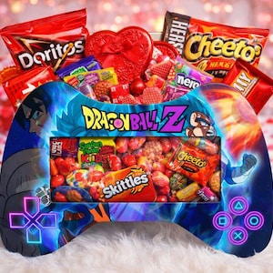 May include: A Valentine's Day gift basket in the shape of a video game controller, with the Dragon Ball Z logo. The basket contains sweets, snacks, and a heart-shaped chocolate box. The controller design is blue and purple.