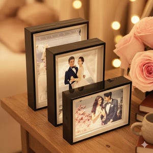 Peut inclure: Trois cadres photo rectangulaires noirs avec des images éclairées de couples. Les cadres sont disposés sur une surface en bois, avec un bouquet de roses roses en arrière-plan. Les cadres ont un interrupteur sur le dessus.
