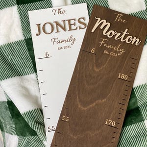 May include: Two white and brown wooden growth charts with the text "The Jones Family Est. 2021" and "The Morton Family Est. 2023" on them. The charts have measurements in inches.