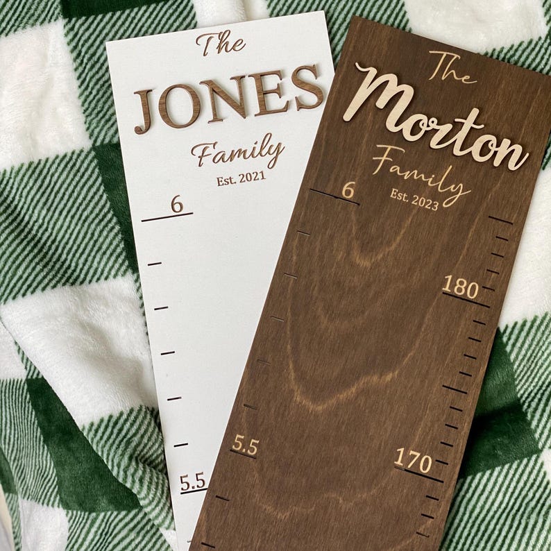 May include: Two white and brown wooden growth charts with the text "The Jones Family Est. 2021" and "The Morton Family Est. 2023" on them. The charts have measurements in inches.
