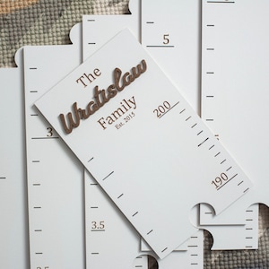 May include: White wooden growth chart with black markings and a brown wooden nameplate that reads "The Wratislaw Family Est. 2015".