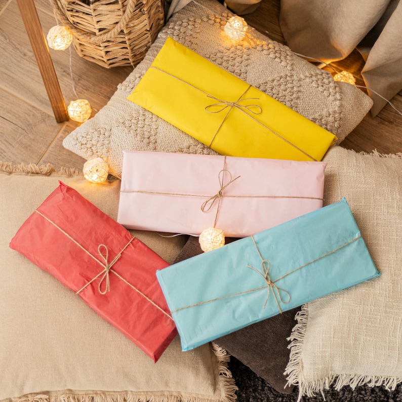 May include: Four wrapped presents in different colours and sizes, tied with twine, on a white and beige textured surface. The presents are surrounded by fairy lights.