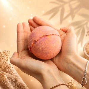 May include: A spherical bath bomb with a textured surface featuring a gradient of orange, pink, and yellow hues. The round object has a visible seam running horizontally across its center, indicating the two halves pressed together during production.