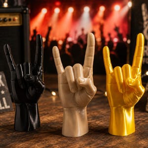 May include: Three hand sculptures in black, beige, and gold, each posed in the rock and roll sign with the index and pinky fingers extended. These upright figures feature realistic anatomical details, including knuckles and fingernails, on a flat base.