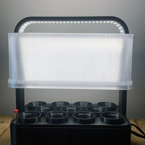 May include: A black indoor hydroponic garden system featuring a rectangular base with nine circular planting slots, a black support frame, and an integrated LED light bar with a translucent white plastic light diffuser panel and a small red float indicator.