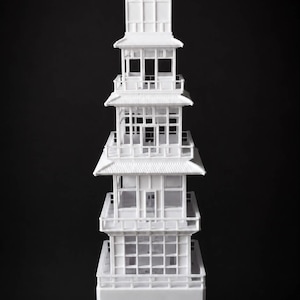 Może przedstawiać: Biały, wielopoziomowy model pagody składający się z czterech kondygnacji z otwartymi ramami okiennymi, balkonami i spiczastym dachem. Ta architektoniczna rzeźba jest osadzona na pojedynczym, centralnym cokole o sześciokątnej podstawie.