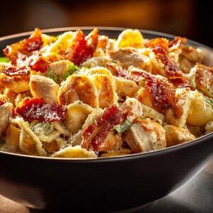 Peut inclure: Gros plan sur un bol noir rempli de pâtes, de poulet et de bacon. Les pâtes sont en forme de coquillage, et le poulet est coupé en morceaux. Des morceaux de bacon croustillants sont dispersés, avec du fromage râpé.