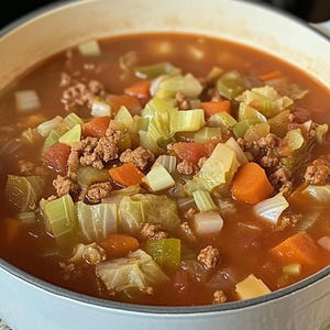 Puede incluir: Una olla blanca llena de una sopa roja a base de tomate con carne picada, col, zanahorias, apio y cebollas.