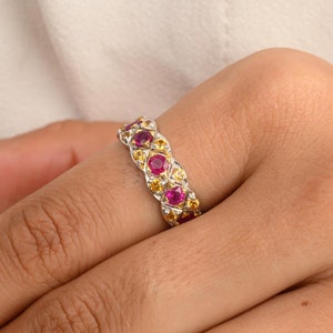 May include: A silver band ring with alternating red and yellow gemstones. The ring is set with round stones and has a polished finish.